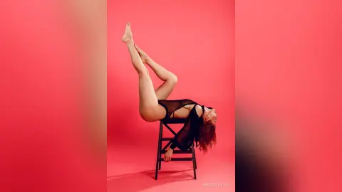 Athletic woman in a black bodysuit performing a backbend on a stool against a vibrant pink studio background.