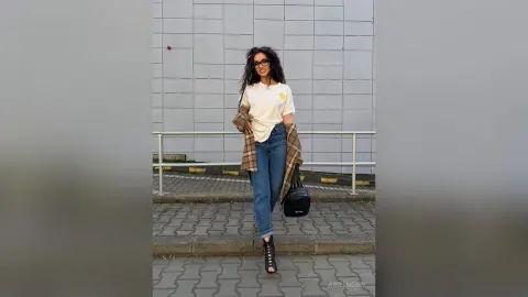Stylish woman in white t-shirt and blue jeans standing by a city railing in a casual urban setting.
