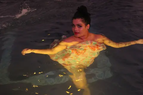 Curvy woman in a floral patterned dress floating peacefully in dark water at night.