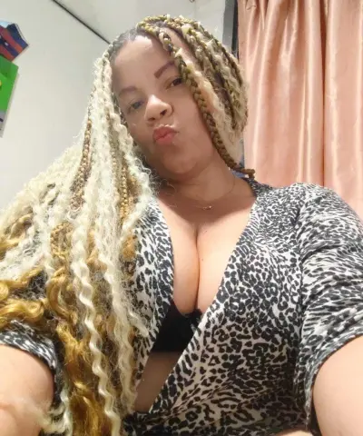 Smiling woman with long blonde braids wearing a leopard print top in a cozy indoor setting.