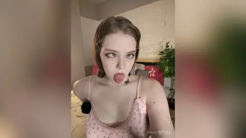 Young woman in a pink floral camisole making a playful expression in a cozy bedroom setting.