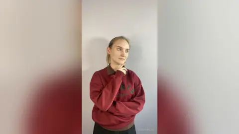 Thoughtful young woman in a burgundy oversized sweatshirt posing against a plain neutral background.