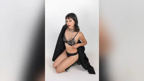 LilithBrooks kneels against a white background wearing black lace lingerie and a black choker.