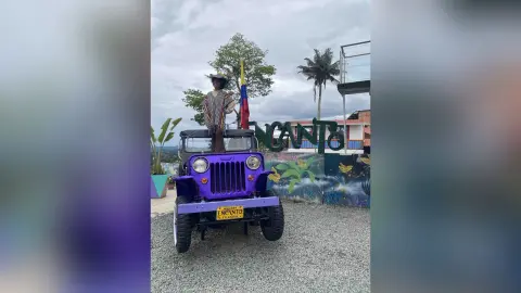 Woman in a striped shirt and hat standing on a purple vintage Jeep in front of an Encanto sign outdoors.