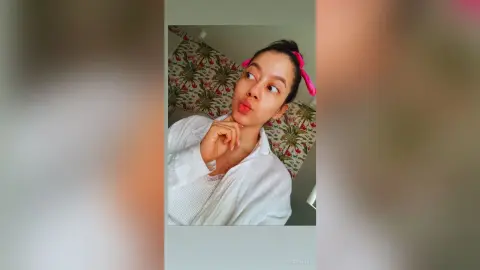 JessieLiu pouts her lips while wearing a white button-down shirt with her dark hair pulled back with a pink scrunchie.