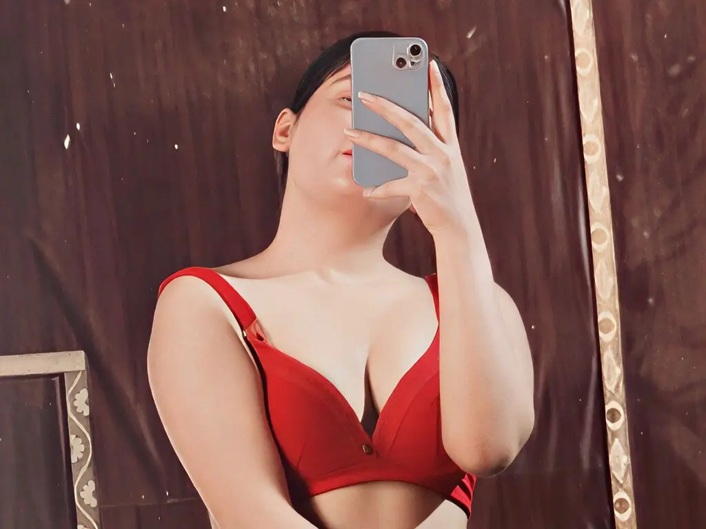 Young woman in a red bra taking a mirror selfie against a dark brown background.