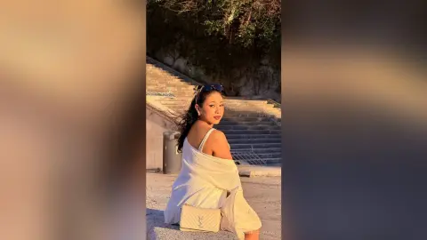 Young woman in a white dress sitting on stone stairs during a warm golden hour sunset.