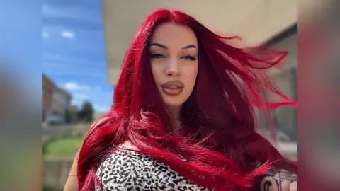 AriaVex poses outdoors with her long red hair blowing in the wind while wearing a leopard print top.