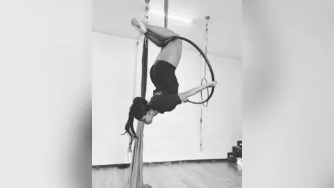 KeianHoz performs an aerial hoop routine, hanging upside down in a black bodysuit with her legs bent behind her.