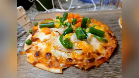 Homemade veggie pizza with melted cheese, green peppers, and corn on a rustic wooden serving board.