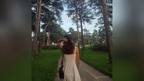Woman in a white polka dot sundress walking through a peaceful pine forest path at dusk.