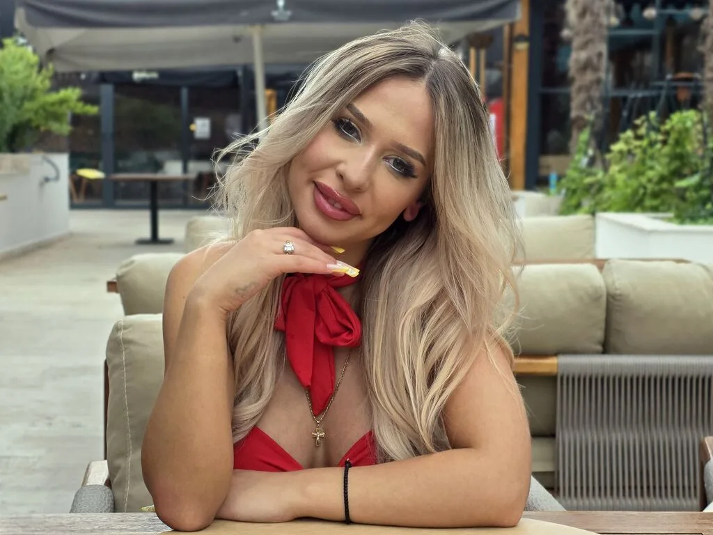 JoRed smiles while sitting at an outdoor cafe wearing a red halter top.