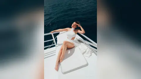 Elegant woman in a white swimsuit relaxing on a luxury yacht deck amidst deep blue ocean waters.