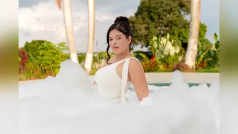 Young woman in a white dress relaxing in a bubbly foam bath at a tropical outdoor resort.