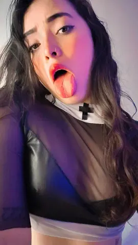 Young woman with long wavy hair wearing a black leather crop top and white collar in soft indoor lighting.