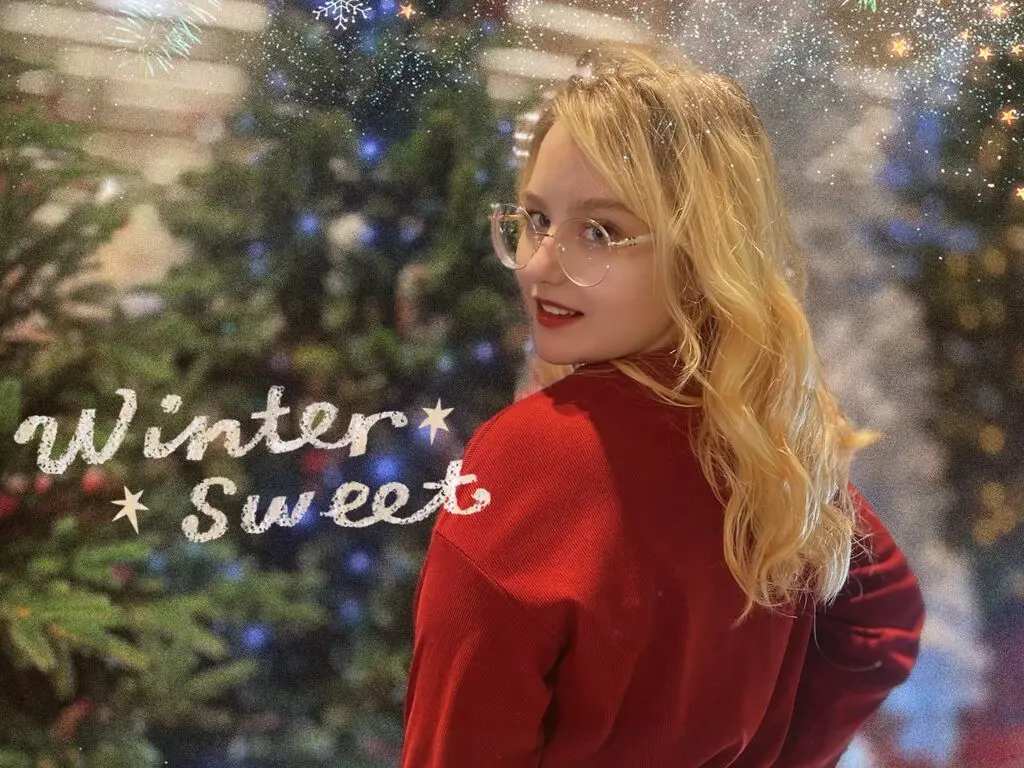 Smiling blonde woman in a red sweater posing in front of a festive winter wonderland background.