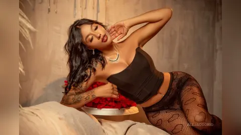 Aleja poses in a black tube top and sheer patterned tights, leaning back against a bed or soft surface.