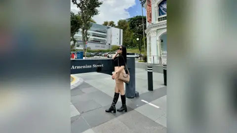 Stylish woman in a black crop top and tall black boots standing on Armenian Street in a sunny urban setting.