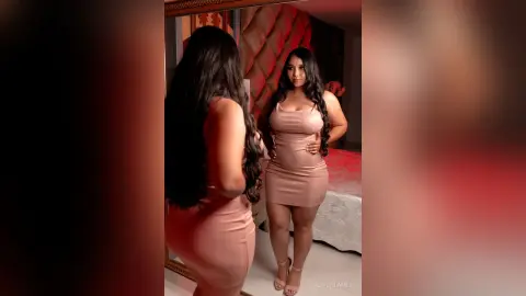 Curvy woman in a tight pink midi dress posing in a bedroom mirror for a glamorous portrait.