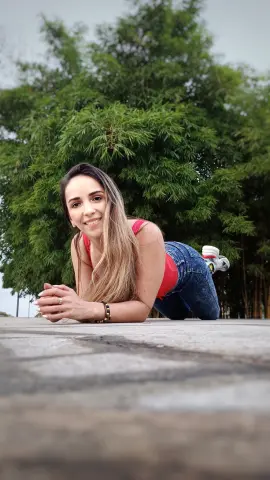 Smiling young woman in a red tank top and blue jeans relaxing outdoors against a lush green bamboo background.