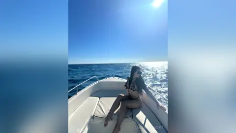 Woman in black bikini relaxing on a white boat under a bright sunny sky on the ocean.