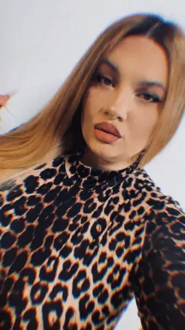 Blonde woman in a stylish leopard print turtleneck top posing against a white background.