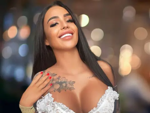 Smiling brunette woman in a white lace outfit with floral tattoos against a soft bokeh city background.