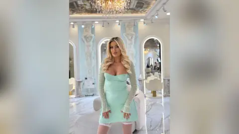 Blonde woman in a mint green sequin long-sleeve dress posing in a luxurious white marble interior.