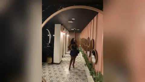KeianHoz stands in a hallway wearing a black lace bodysuit, posing in front of a wall of round mirrors.