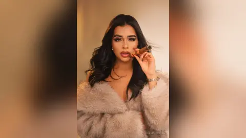 Glamorous woman in a beige faux fur coat smoking a cigar against a warm studio background.