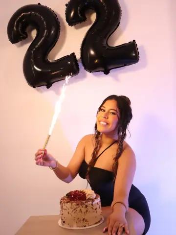Smiling woman in a black dress celebrating her 22nd birthday with a cake and sparkling candle.