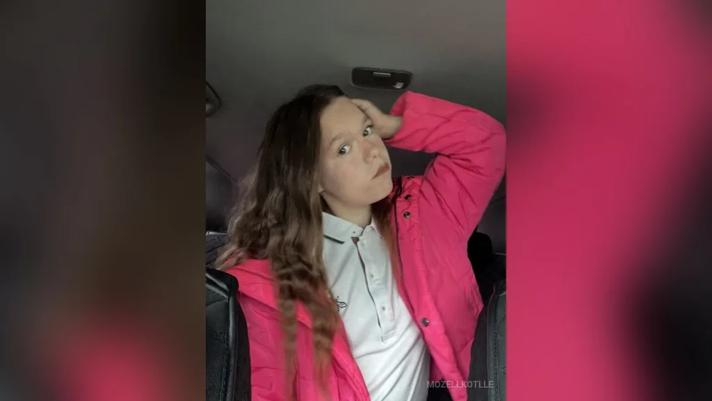 MozellKotlle poses in a bright pink puffer jacket with her hand resting in her long brown hair.