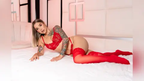 Blonde woman in red lace lingerie and stockings relaxing on a white bed in a bright pink bedroom.