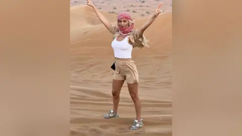 Joyful woman in white tank top and tan shorts celebrating in a vast desert landscape.