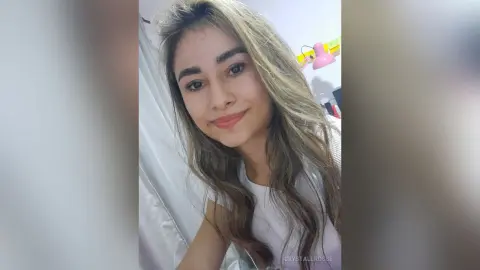 CrystallRosse smiles at the camera with her long blonde hair while wearing a white top.