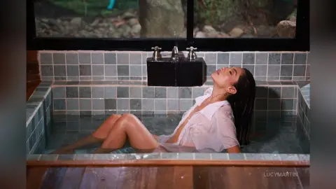 LucyMartin relaxes in a tiled hot tub wearing an open white button-down shirt with her wet hair slicked back.