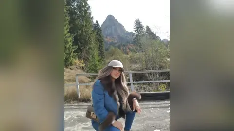 Stylish woman in a denim jacket and beige cap sitting on a mountain overlook during a scenic autumn hike.