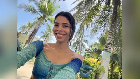 Smiling woman in a blue textured summer top relaxing amidst tropical palm trees on a sunny day.