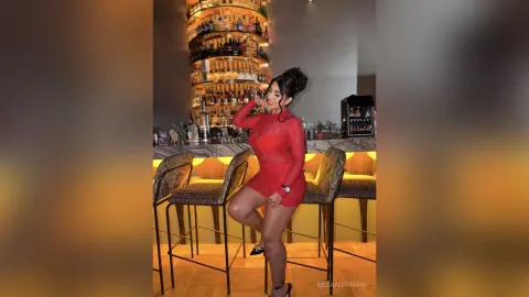 Stylish woman in a red lace cocktail dress posing at a modern bar with warm ambient lighting.