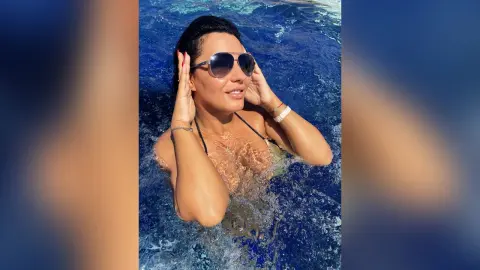 MissyJolie wears sunglasses and smiles while neck-deep in blue swimming pool water.