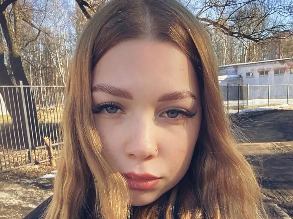 Close-up portrait of a young woman with long blonde hair outdoors in natural sunlight.