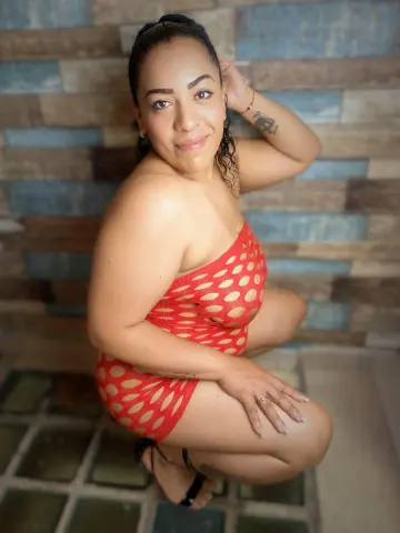 Smiling woman in a red polka dot mini dress posing against a rustic wood paneled wall.