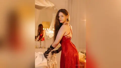 Elegant woman in a red sequin evening gown posing in a warm, glamorous indoor setting.