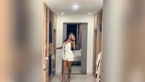 Young woman in a white summer romper taking a mirror selfie in a modern minimalist bedroom.