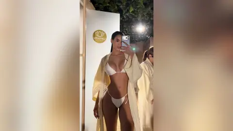 Alison poses for a mirror selfie wearing a white bikini and an open white robe.