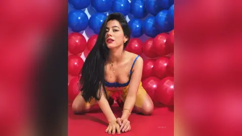 JessieLiu poses in a blue lace bra and yellow skirt against a background of red and blue balloons.