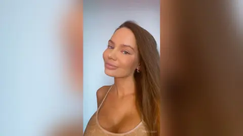 Smiling woman in a beige sparkly camisole top posing against a soft white background.