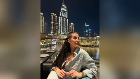 Stylish woman in a light blue denim shirt enjoying a glamorous night out overlooking the Dubai skyline.