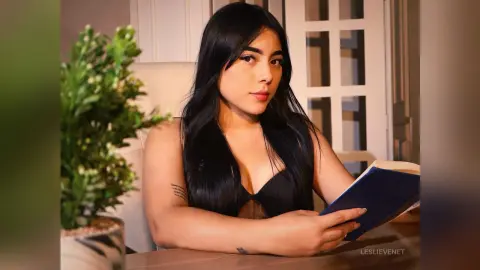 Young woman with long dark hair in a black top reading a book in a cozy indoor setting.