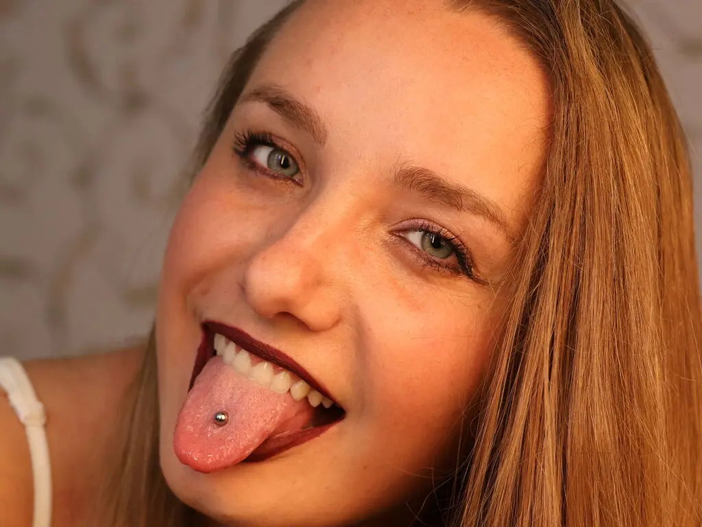 Smiling young woman with blonde hair and tongue piercing in a warm, close-up portrait.
